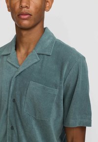 Korte mouw, knoopsluiting shirt van zacht teal stof. Bevat een borstzak, puntige kraag en gestructureerde afwerking.