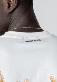 White cotton T-shirt with "MORATO" logo in black at the back neck, featuring subtle texture and a smooth finish. Silver chain visible.