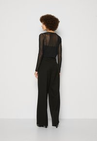 Black mesh long-sleeve top paired with wide-leg black trousers. The outfit features a smooth texture and form-fitting design.