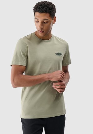 Jasnozielona bawełniana koszulka z okrągłym dekoltem i krótkimi rękawami. Posiada mały nadruk graficzny na klatce piersiowej. Gładka tekstura.