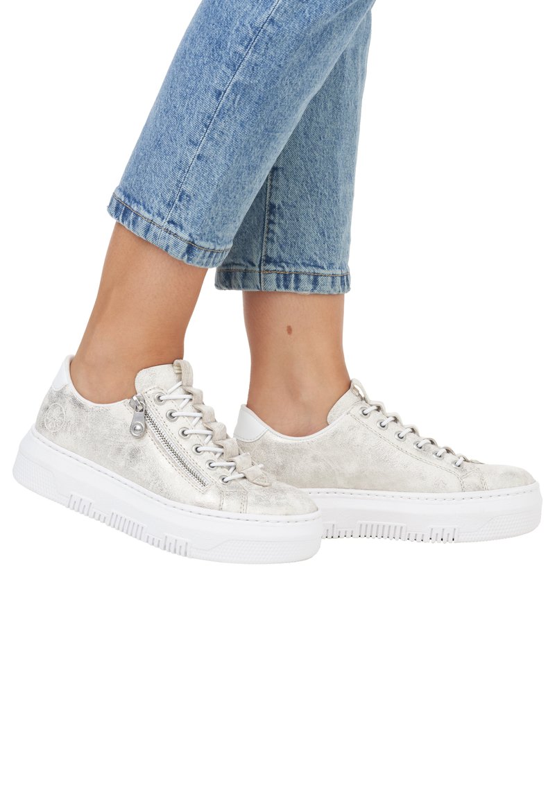 Baskets argentées métalliques avec une finition texturée, semelle en caoutchouc blanche et détail de zip sur le côté. Associées à un jean cropped bleu clair.