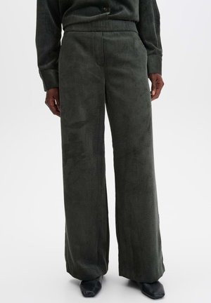 Personne portant un pantalon large en velours côtelé gris foncé avec un haut à manches longues sombre assorti et des chaussures noires à bout carré.