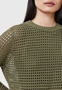 Suéter de punto verde con un diseño de celosía. Presenta un escote redondo y un patrón texturizado con detalles de calados en las mangas.