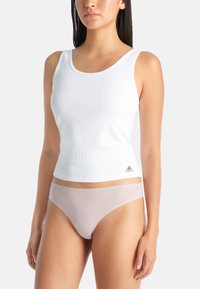 Bílý žebrovaný tílko s kulatým výstřihem a logem Adidas na lemu. V kombinaci se světle růžovým bezešvým prádlem. Hladká textura.