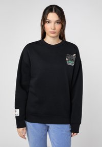 Schwarzer Sweatshirt mit Rundhalsausschnitt, ausgestattet mit grafischem Text auf der Brust und einem Etikett am Ärmel. Weicher Stoff mit lockerer Passform.