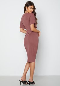 Taille ajusterende midi-jurk in mauve stof met korte mouwen, ronde halslijn en een gladde textuur; gecombineerd met zwarte hoge hakken.