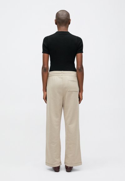 Čierny rebrovaný top s krátkymi rukávmi a priliehavým strihom v kombinácii s béžovými širokými teplákmi s vreckom vzadu a elastickým pásom.