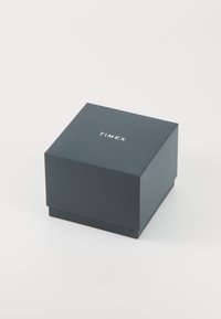 Boîte de montre Timex, en forme carrée, en carte noire matte de couleur bleu foncé, avec un texte blanc sur le dessus, au design simple et épuré.
