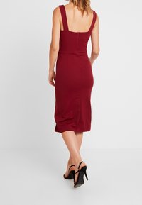 Burgundy muotoonommeltu mekko leveillä olkaimilla, takana vetoketju, polvipituinen helma ja hienovarainen sivusomistus. Yhdistetty mustiin korkokenkiin.