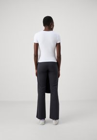 White fitted t-shirt with short sleeves paired with black, flared pants featuring a side slit, worn with white sneakers.