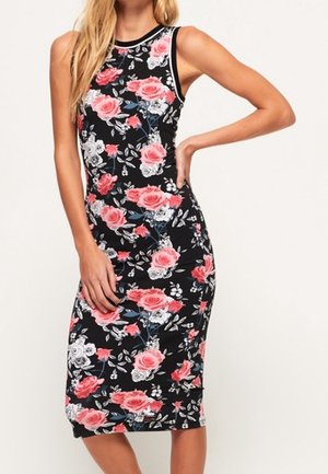 Vestido midi negro sin mangas con estampado floral de rosas en rosa, rojo y blanco, llevado por una mujer con una mano en la cadera.