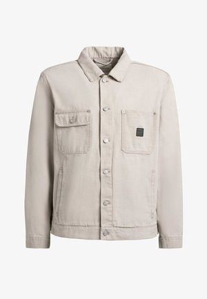 Helebeežimpruun särgivarrukaga jakk kraega, kahe rindtaskuga—üks klapi ja nupuga, teine logomärgiga—ning küljetaskutega.