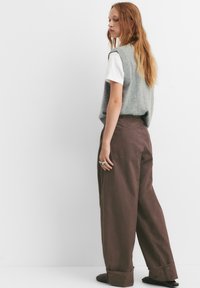 Grijze gebreide vest over een witte shirt met korte mouwen, gecombineerd met losse, bruine wijde broekspijpen. Gladde texturen zonder zichtbare patronen.