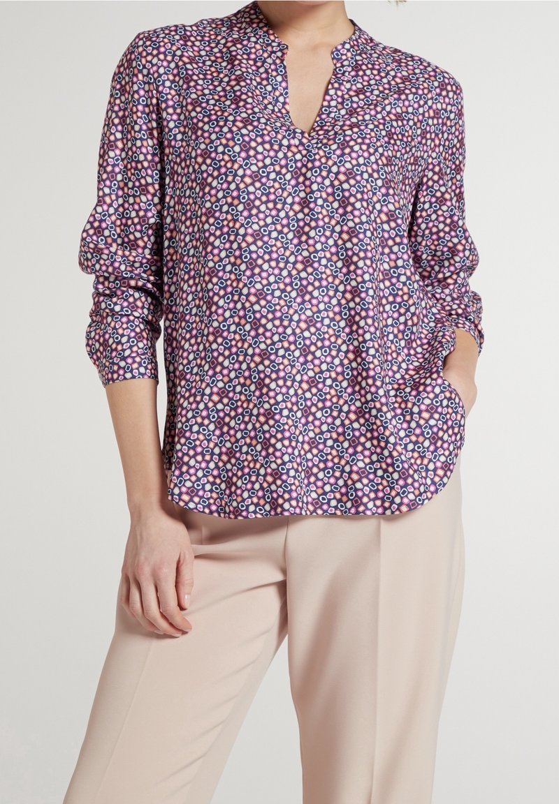 Blouse à motifs violets avec un col en V, manches longues et une coupe décontractée. Présente un imprimé géométrique aux tons roses et bleus.