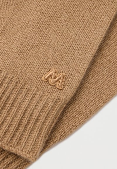 Strickpulli aus tanfarbenem Wolle mit gerippten Bündchen. Verfügt über ein kleines, gesticktes tanfarbenes 'M'-Logo nahe dem Bündchen. Weiche Textur.