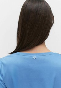 Blå bomullströja med rund halsringning, som har en liten detalj i silverring i ryggen. Mjuk textur och enkel design.