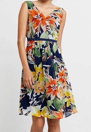 Robe sans manches longueur genou avec décolleté en V, base bleu marine, et grand motif floral aux teintes orange, jaune, vert et blanc, avec une taille cintrée.