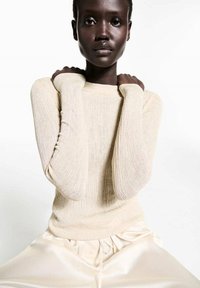 Maglione a coste color beige chiaro con maniche lunghe, caratterizzato da una vestibilità comoda e scollatura rotonda. Abbinato a pantaloni in satin con coulisse.