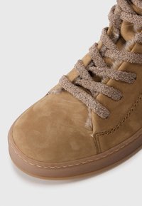 Botín de ante marrón con forro de piel suave, cordones texturizados marrones y suela de goma. Detalles de costura a lo largo del borde.