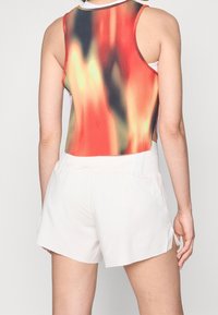 Débardeur côtelé dégradé rouge, orange et vert, associé à un short blanc en tissu doux jusqu'aux genoux avec des fentes sur les côtés et une taille élastique.