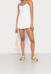 Bílé šaty s malým žlutým květinovým potiskem, nařasený živůtek, tenká ramínka a rozšířená sukňa. V kombinaci se žlutými sandály a malou kabelkou.