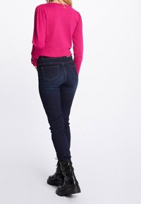 Top fucsia a maniche lunghe abbinato a jeans skinny blu scuro e stivaletti neri. Il top presenta maniche pompose e dettagli di bottoni.