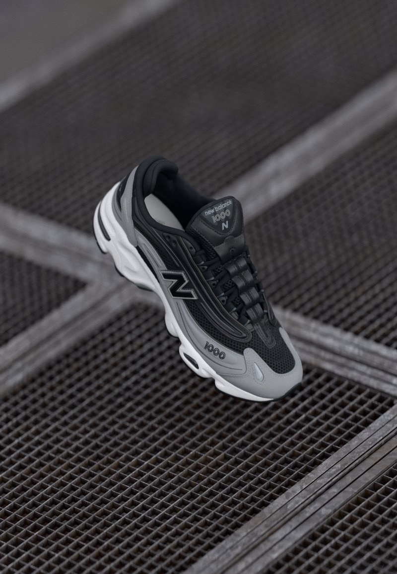 Black and gray New Balance 1000 sneaker suspended over a metal grid floor with white accents and black laces.