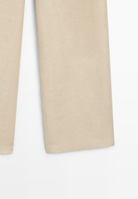 Pantalon beige droit, coupé à la cheville, avec des coutures visibles sur fond blanc.