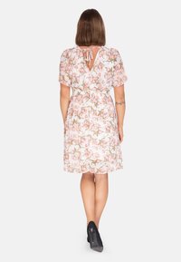 Blumenkleid mit kurzen Ärmeln, tailliertem Schnitt und Schlüsselrücken. Präsentiert pinke und grüne Blumenmuster auf weißem Hintergrund.