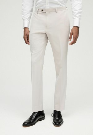 Pantalones de vestir color beige claro con un corte ajustado, parte frontal plana, pasadores para cinturón y cierre de un solo botón. Combinados con zapatos de vestir de piel negra.