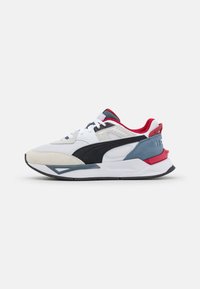 Scarpa da ginnastica bianca, nera e grigia realizzata con materiali in rete e suede. Presenta dettagli rossi e una suola spessa con una finitura texturizzata.