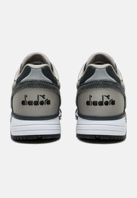 Scarpe sportive grigie e nere con tomaia in tessuto morbido, tallone rinforzato e suola intermedia bianca. Logo "diadora" impresso sul retro.