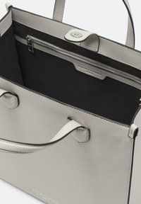 Jasnoszara skórzana torebka o usztywnionym kształcie, z czarnym wnętrzem, uchwytami u góry i zamykaną na zamek kieszenią.