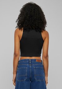 Svart kort topp med en åtsittande design, kombinerad med högmidjade blå denimjeans som har två bakfickor och en läderetikett.