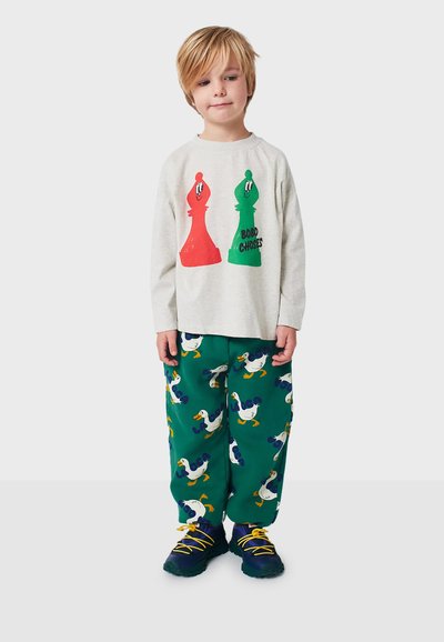 Long-sleeve gray shirt with red and green chess piece graphics, paired with green pants featuring duck patterns and yellow laces on shoes.