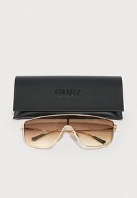 Γυαλιά ηλίου aviator με χρυσή κορνίζα και καφέ φακούς με διαβάθμιση, τοποθετημένα κάτω από μια μαύρη θήκη γυαλιών με το λογότυπο QUAY, σε λευκό φόντο.