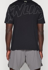 Camiseta de algodón negra con gran texto gráfico blanco en la parte posterior. La camiseta tiene mangas cortas y un escote redondo.