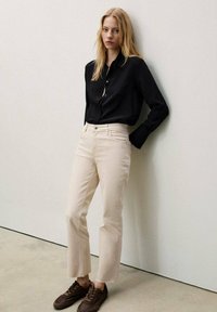 Zwarte button-up shirt, beige rechte broek met een ruwe zoom, en bruine sneakers. Glad stof met minimale details.