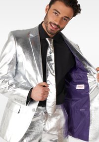 Shiny silver suit with matching tie, featuring a purple inner lining and brand label. Smooth texture and tailored fit are evident.