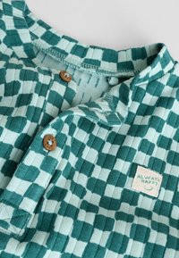 Turquoise geruiten shirt, geribde textuur, met houten knopen en een klein "Always Happy" label. Zachte katoenen stof, ronde halslijn.