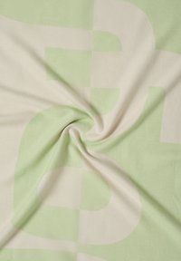 Bomuldstæppe med et stort abstrakt mønster i lysegrøn og cremefarve. Blød tekstur med et glat, flydende udseende.