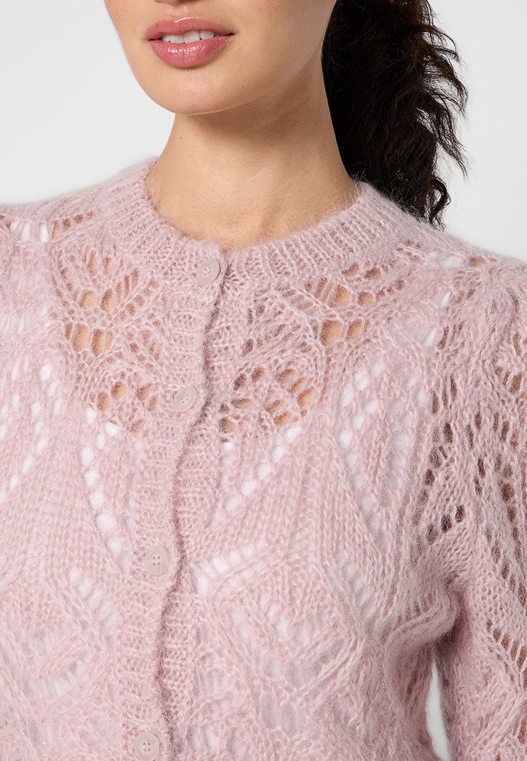 Jasnoróżowy sweter robiony na drutach z misternym wzorem koronkowym, okrągłym dekoltem i zapięciem na guziki. Miękki, teksturowany materiał z otwartymi oczkami.