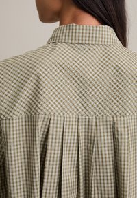 Groene en beige geruite blouse met een kraagnek en geplooid achterontwerp, gemaakt van lichtgewicht stof met een gestructureerde afwerking.