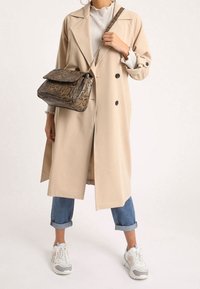 Vaaleanbeige sadetakki, jossa on kaksirivinen malli, yhdistettynä vaaleansinisiin kulutettuihin farkkuihin. Tummakuosiset laukku, jossa on läppä ja ketjuhihna, sekä valkoiset lenkkitossut.