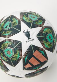 Witte voetbal met zwarte hexagonale panelen, voorzien van groene accenten, trofee-logo en een gestructureerd oppervlak. Opvallende inscriptie "Munich 25".