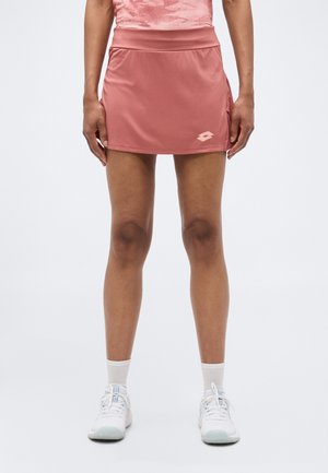 Woman wearing a pink athletic skirt and top, white socks, and white sneakers, standing with arms relaxed by her sides.