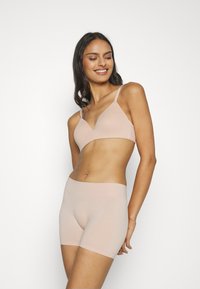 Light pink seamless bra with triangular cups and adjustable straps, paired with matching seamless shorts, both made from soft stretch fabric.