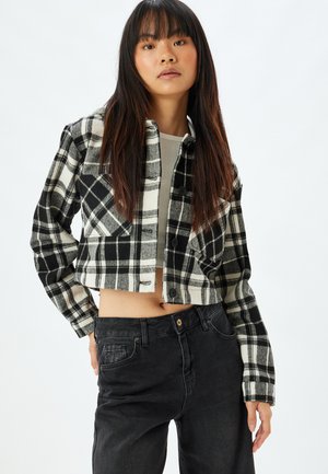 Kort flanellen jack in zwart-wit blokpatroon, met knoopsluitingen en lange mouwen, gecombineerd met zwarte denim jeans.