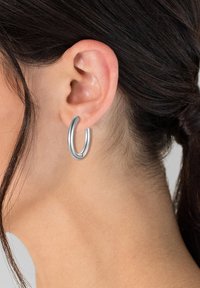 Silberne Creolen mit einer glatten, glänzenden Oberfläche, die ein nahtloses Design und eine leicht verlängerte ovalen Form aufweisen.
