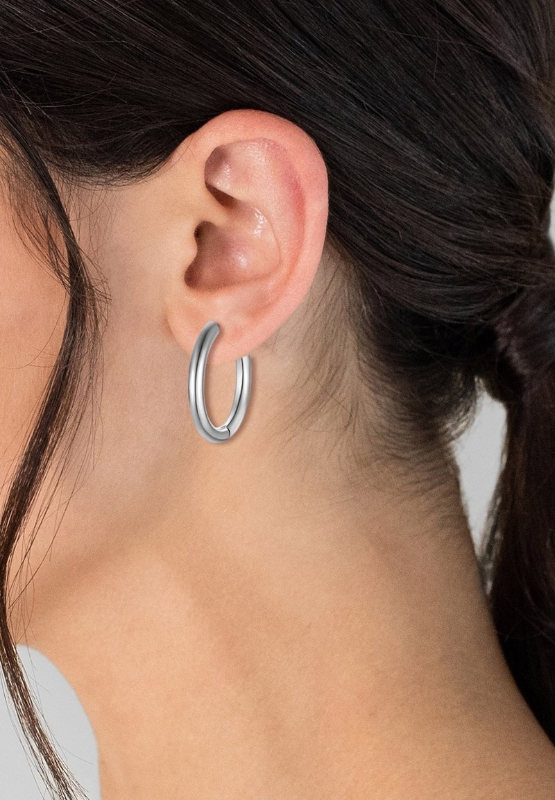 Silberne Creolen mit einer glatten, glänzenden Oberfläche, die ein nahtloses Design und eine leicht verlängerte ovalen Form aufweisen.